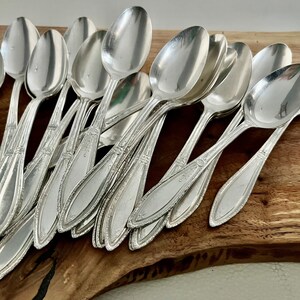 K&ouml;nnte beinhalten: Ein Set antiker Silberl&ouml;ffel mit verzierten Details. Die L&ouml;ffel liegen auf einer Holzoberfl&auml;che.