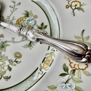 K&ouml;nnte beinhalten: Eine wei&szlig;e Keramik-Tasse mit schwarzem Henkel und dem Text "But First, Coffee" in schwarzer, fetter Schrift. Die Tasse steht auf einer wei&szlig;en Oberfl&auml;che.