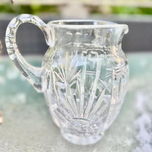 Puede incluir: Una jarrita de cristal tallado transparente con asa y boquilla. La jarrita presenta un detallado dise&ntilde;o de estrella en el cuerpo y el asa. El cristal es transparente, permitiendo el paso de la luz.