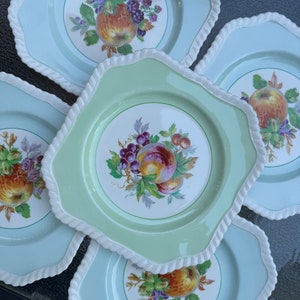 Puede incluir: Juego de cuatro platos de cer&aacute;mica vintage con esmalte verde y azul. Cada plato presenta un dise&ntilde;o de fruta diferente con un borde blanco.