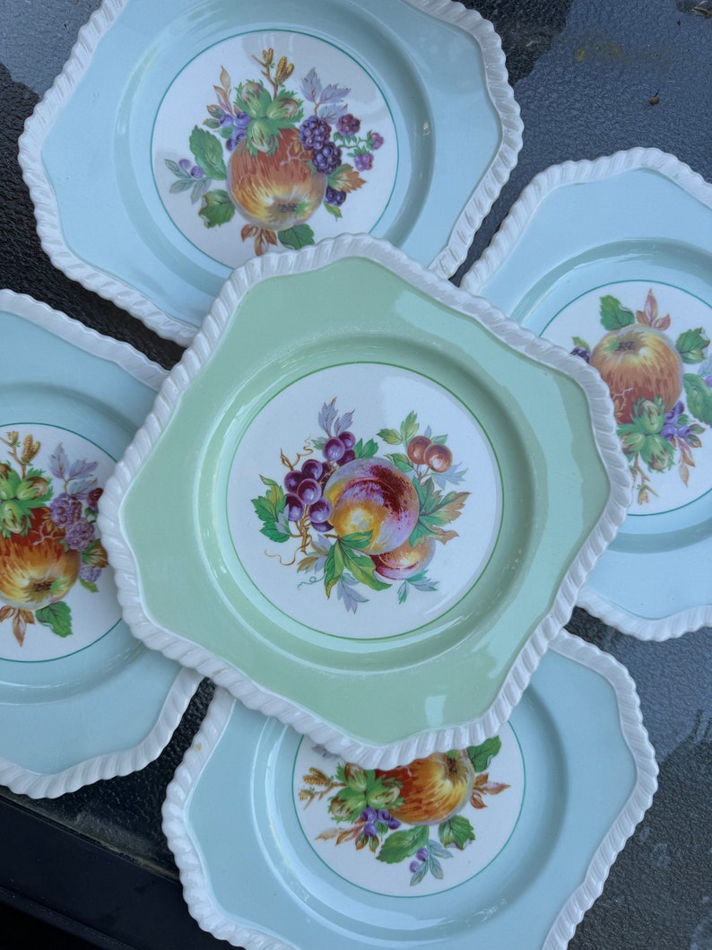 Puede incluir: Juego de cuatro platos de cer&aacute;mica vintage con esmalte verde y azul. Cada plato presenta un dise&ntilde;o de fruta diferente con un borde blanco.