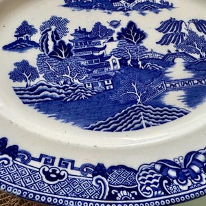 K&ouml;nnte beinhalten: Blau-wei&szlig;e Porzellanplatte mit traditionellem chinesischem Landschaftsdesign. Die Platte zeigt eine Pagode, B&auml;ume, eine Br&uuml;cke und einen Fluss. Der Rand der Platte ist mit einem sich wiederholenden geometrischen Muster verziert.