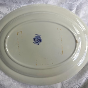 May include: An oval-shaped white ceramic serving platter with a smooth, glossy finish. The underside features a blue printed maker's mark that reads Willow Wood & Sons England. There are two faint, rectangular orange-toned marks on the surface.