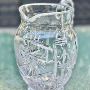 Puede incluir: Una jarra de cristal tallado transparente con asa y pico vertedor. La jarra presenta un patr&oacute;n detallado de estrellas y formas geom&eacute;tricas. El vidrio es grueso y refleja la luz, creando un efecto brillante.