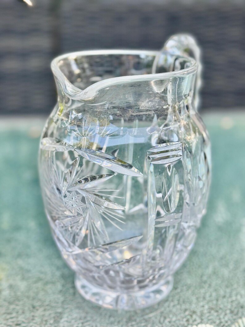 Puede incluir: Una jarra de cristal tallado transparente con asa y pico vertedor. La jarra presenta un patr&oacute;n detallado de estrellas y formas geom&eacute;tricas. El vidrio es grueso y refleja la luz, creando un efecto brillante.