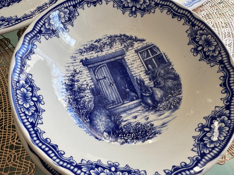 K&ouml;nnte beinhalten: Eine blaue und wei&szlig;e Keramiksch&uuml;ssel mit einem Cottage- und Kaninchen-Design. Die Sch&uuml;ssel hat einen gewellten Rand und ein blaues Blumenmuster.