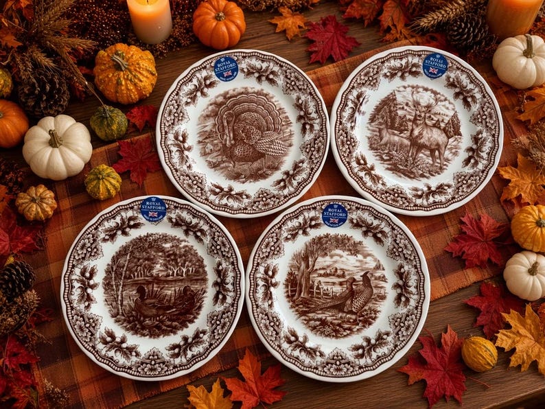 Op de afbeelding: Vier witte keramische borden met bruine transferware-ontwerpen met een kalkoen, een hert, eenden en fazanten. Elk bord heeft een geschulpte rand en een Royal Stafford-sticker. De centrale illustraties zijn omringd door een gedetailleerde bloemenrand.