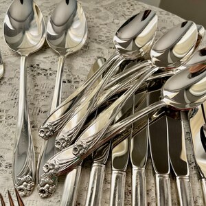 May include: A set of silverware with a floral design on the handles. The silverware includes spoons, forks, and knives. The silverware is made of polished silver.