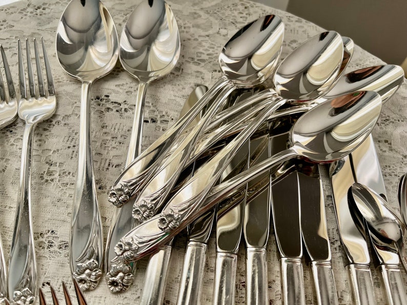 May include: A set of silverware with a floral design on the handles. The silverware includes spoons, forks, and knives. The silverware is made of polished silver.
