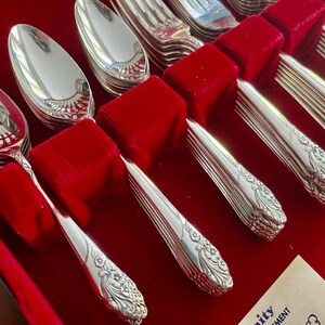 May include: A set of polished silverware, including spoons and forks, arranged in a red velvet-lined case. The silverware has a floral design on the handles. The spoons and forks are neatly organized, reflecting light. The overall presentation suggests a formal dining set.