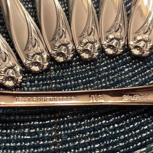 May include: Close-up of the back of a silver fork with the inscription "1847 Rogers Bros." and "18" stamped on the back. The fork has a floral design with a flower at the end of the handle.
