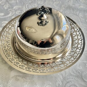 May include: Silver-plated butter dish with a domed lid and intricate openwork design on the base. The lid features a decorative handle. The dish is designed to hold butter and is suitable for serving.