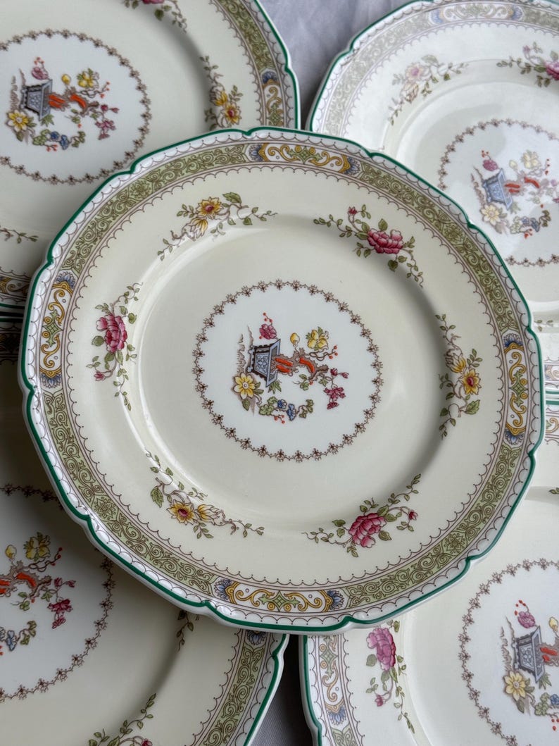 Puede incluir: Juego de cuatro platos de cena de porcelana blanca vintage con un patr&oacute;n floral verde y dorado. Los platos tienen un borde festoneado y un delicado dise&ntilde;o floral.