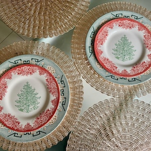 May include: Overhead shot of a table setting with four place settings. Each setting includes a gold-colored placemat, a green and white patterned plate, and a smaller plate with a red floral border and a green Christmas tree design.