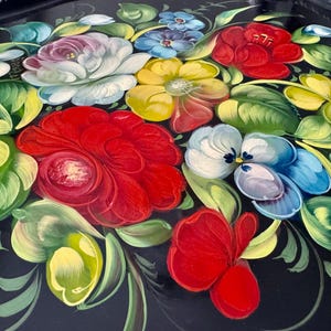 May include: A black decorative tray with a vibrant floral design. The flowers are painted in shades of red, yellow, white, blue, and green, with detailed brushstrokes. The tray's edges have a gold trim.