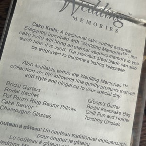 May include: A white card with black text describing a cake knife and other wedding accessories. The text reads "Wedding MemoriesTM" and lists items such as "Bridal Garters", "Groom's Garter", "Bridal Sachet", "Bridal Keepsake Bag", "Pot Pourri Ring Bearer Pillows", "Quill Pen and Holder", "Cake Server", "Toasting Glasses", and "Champagne Glasses".