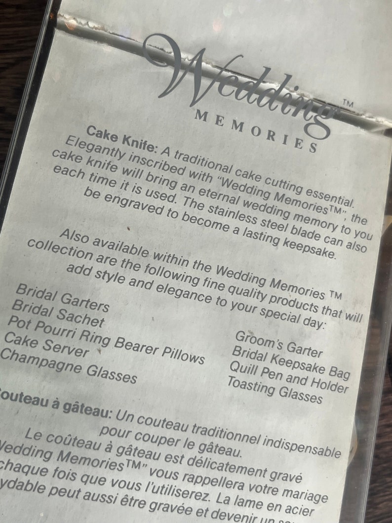 May include: A white card with black text describing a cake knife and other wedding accessories. The text reads "Wedding MemoriesTM" and lists items such as "Bridal Garters", "Groom's Garter", "Bridal Sachet", "Bridal Keepsake Bag", "Pot Pourri Ring Bearer Pillows", "Quill Pen and Holder", "Cake Server", "Toasting Glasses", and "Champagne Glasses".