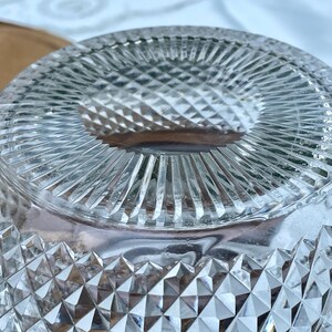 May include: Close-up of a clear glass bowl with a diamond-cut pattern. The bowl's rim features a series of vertical lines, and the base has a diamond-shaped design. The bowl is likely used for serving or display.