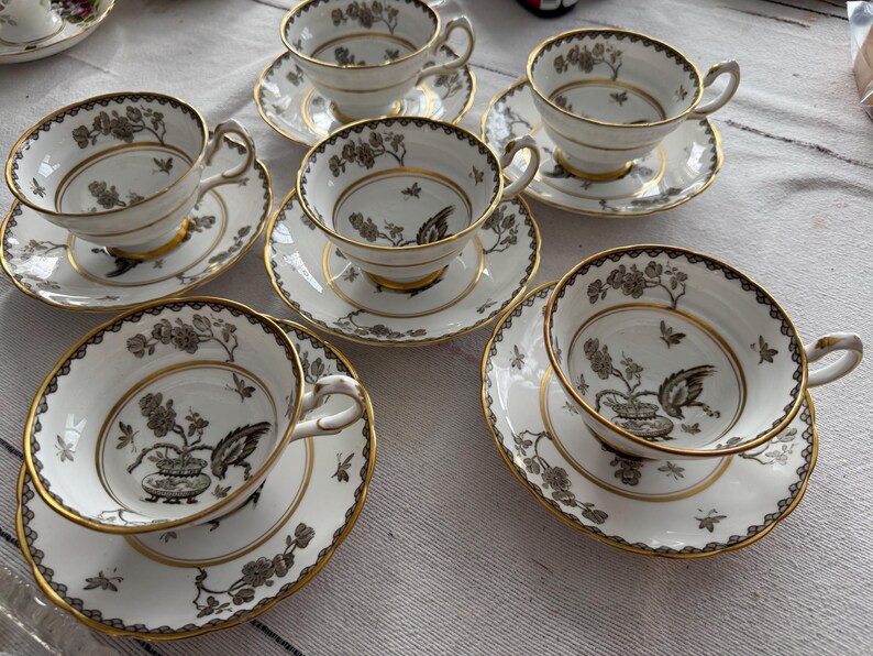 May include: Set of six teacups and saucers with a black and white floral pattern and gold trim. The cups and saucers are made of fine china.
