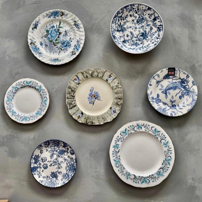 Op de afbeelding: Een verzameling van zes ronde keramische borden met diverse blauw-witte bloemen-, botanische en vogelpatronen. De borden vari&euml;ren in grootte en randafwerking, inclusief geschulpte en gladde randen, waarbij &eacute;&eacute;n bord een klein zwart label bevat.
