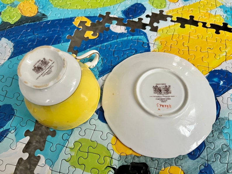 Pu&ograve; includere: Un set di tazza e piattino giallo e bianco in porcellana fine. Il lato inferiore della tazza e del piattino presenta un marchio del produttore Paragon stampato in nero con il testo H.M. THE QUEEN & H.M. QUEEN MARY FINE BONE CHINA ENGLAND REG'D.