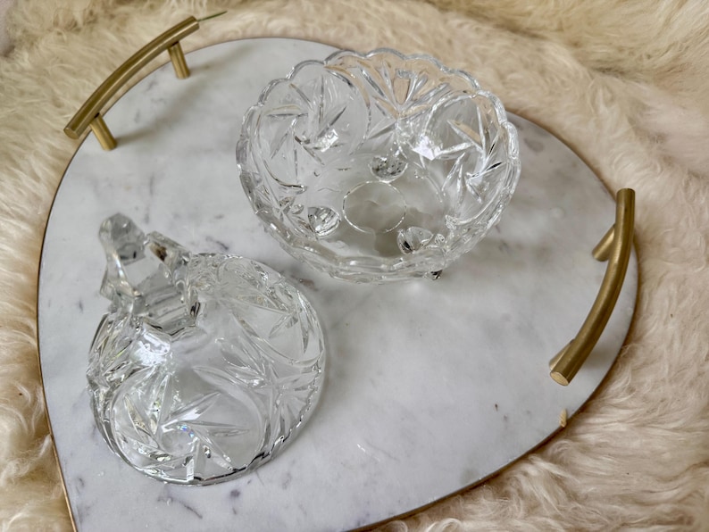 May include: A heart-shaped white marble serving tray with gold-toned metal handles, featuring a clear glass candy dish with a matching lid. The glass dish has a faceted starburst pattern and sits on small feet, displayed with the lid removed.
