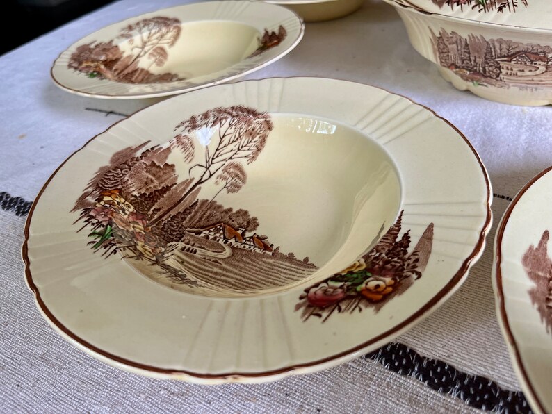 May include: A set of four vintage cream-coloured soup bowls with a brown and green woodland scene design. The bowls have a scalloped edge and a raised rim.