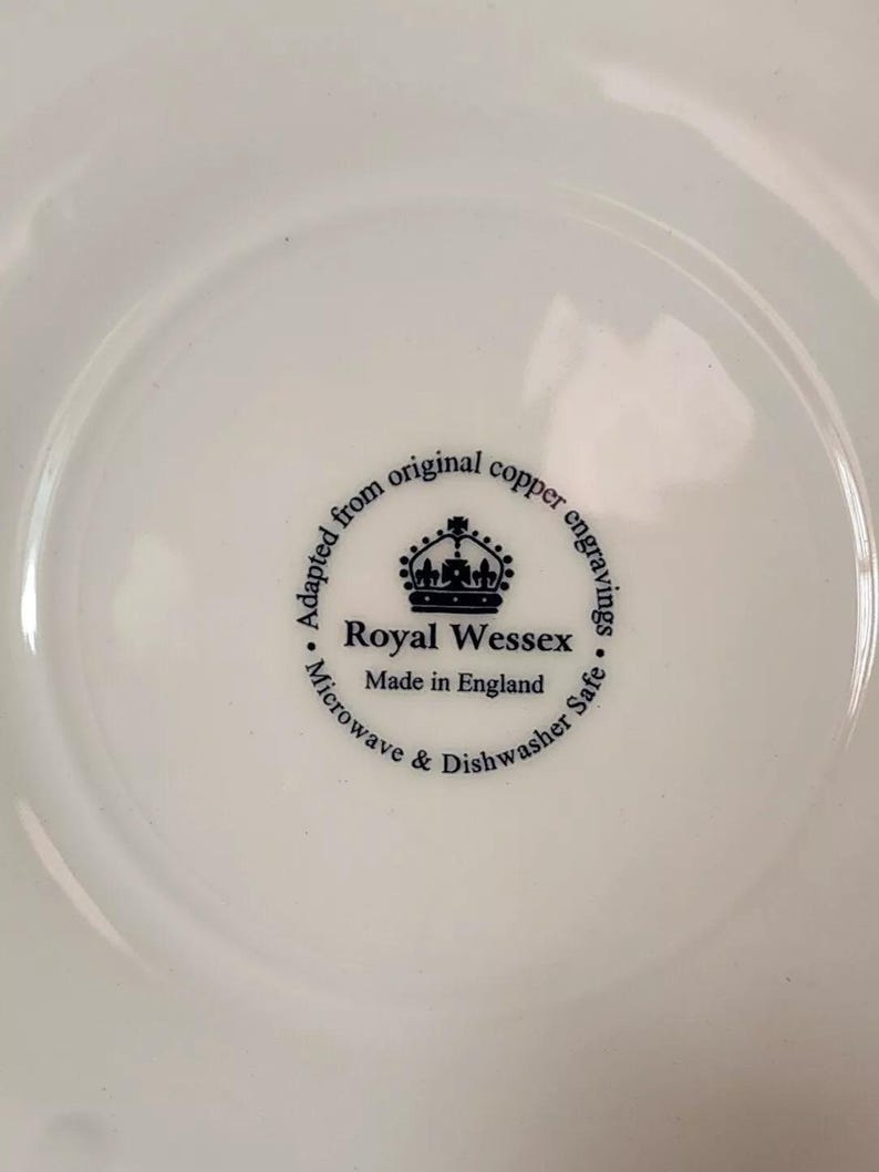K&ouml;nnte beinhalten: Nahaufnahme der Unterseite eines wei&szlig;en Keramiktellers mit einem schwarz-wei&szlig;en Logo, auf dem steht "Adapted from original copper engravings. Royal Wessex. Made in England. Microwave & Dishwasher Safe."