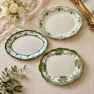 Peut inclure: Trois plats ovales en céramique avec un centre blanc et un bord festonné orné d'un motif floral et de guirlandes vertes. Les assiettes ont une finition brillante et sont disposées sur une surface plane, révélant des détails botaniques.