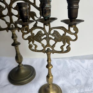 Pu&ograve; includere: Due candelabri antichi in ottone. I candelabri presentano un design dettagliato con figure di leoni. Hanno una base rotonda e uno stelo decorativo. I candelabri sono in stile vintage.