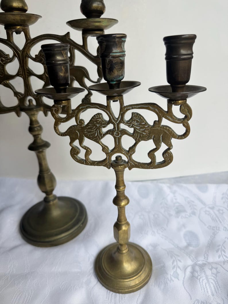 Pu&ograve; includere: Due candelabri antichi in ottone. I candelabri presentano un design dettagliato con figure di leoni. Hanno una base rotonda e uno stelo decorativo. I candelabri sono in stile vintage.