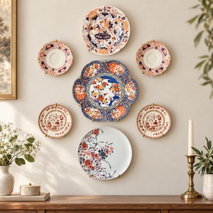 Pu&ograve; includere: Una collezione di sette piatti decorativi in ceramica montati su una parete in una disposizione simmetrica. I piatti presentano intricati motivi floreali e botanici nei toni del blu, rosso, arancione e bianco, con bordi vari e smerlati.