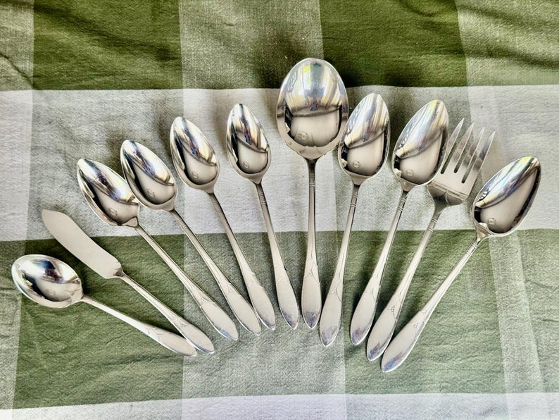 May include: A collection of ten silver-toned stainless steel utensils including one butter knife, one serving spoon, one fork, and seven spoons of varying sizes. Each piece features a smooth, polished finish with a simple, tapered handle design.