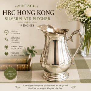 May include: A silverplate pitcher by HBC Hong Kong measuring 9 inches in height. The pitcher features a polished metallic finish, a curved handle, a wide pouring spout with an integrated ice guard, and a circular base. The surface is reflective.