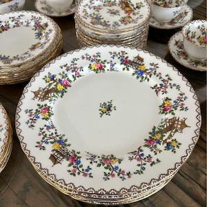 K&ouml;nnte beinhalten: Ein Set Vintage-Porzellan-Geschirr mit einem floralen Muster mit rosa, gelben und blauen Blumen, gr&uuml;nen Bl&auml;ttern und goldenen Akzenten. Das Muster enth&auml;lt ein Pagoden-Design.