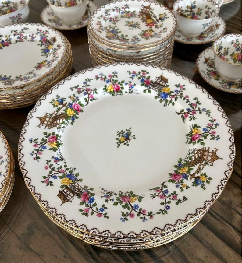K&ouml;nnte beinhalten: Ein Set Vintage-Porzellan-Geschirr mit einem floralen Muster mit rosa, gelben und blauen Blumen, gr&uuml;nen Bl&auml;ttern und goldenen Akzenten. Das Muster enth&auml;lt ein Pagoden-Design.