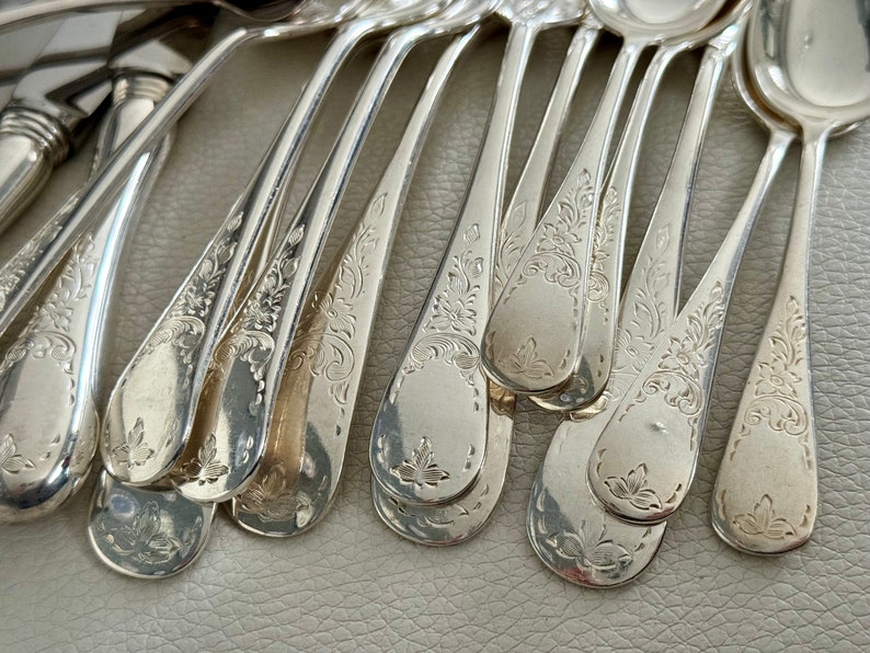 May include: Close-up of a collection of ornate silver spoons. Each spoon features a detailed floral pattern on the handle and bowl. The spoons are arranged in a fan-like pattern, showcasing their elegant design.