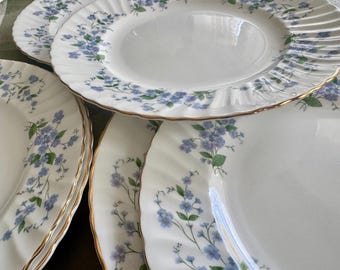 May include: A collection of white porcelain plates with a delicate floral pattern in blue and green. The plates have a gold trim and a scalloped edge. The plates are arranged in a stack, showcasing the intricate design and elegant style.