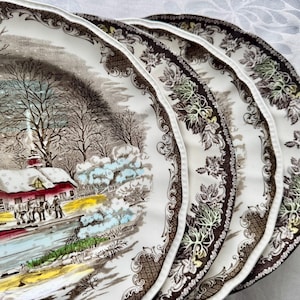 May include: Set of four white ceramic dinner plates with a brown floral pattern and a winter scene with a red house and snow. The plates have a scalloped edge.