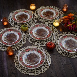 K&ouml;nnte beinhalten: Eine Thanksgiving-Tischdekoration mit sechs Gedecken, Tellern mit Truthahn-Motiv, geflochtenen Tischsets und Kerzen.