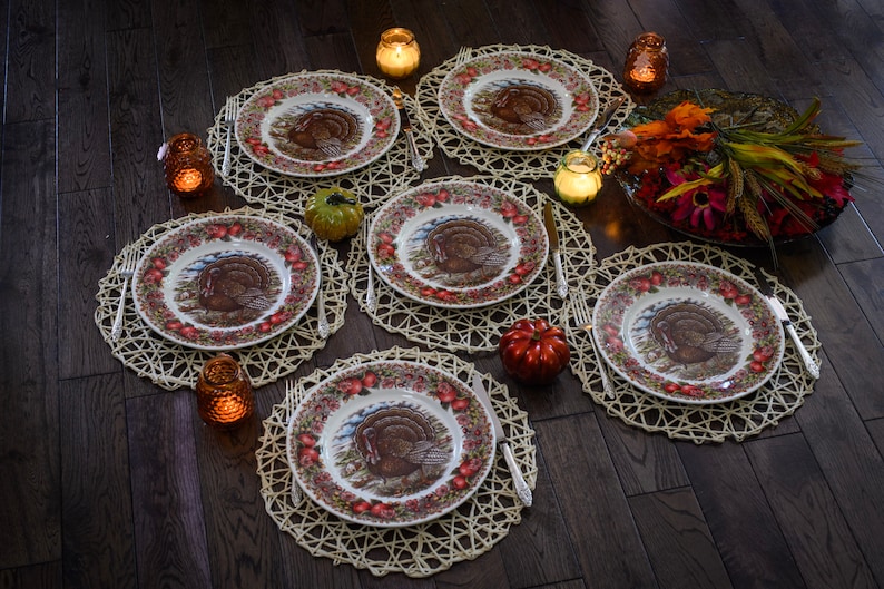 K&ouml;nnte beinhalten: Eine Thanksgiving-Tischdekoration mit sechs Gedecken, Tellern mit Truthahn-Motiv, geflochtenen Tischsets und Kerzen.