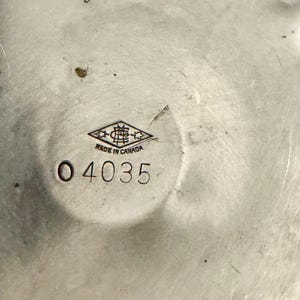 Peut inclure: Gros plan sur un objet m&eacute;tallique argent&eacute; avec un motif circulaire. Le texte "MADE IN CANADA" est visible, ainsi que le num&eacute;ro "04035". L'objet a une surface textur&eacute;e et semble &ecirc;tre vintage.