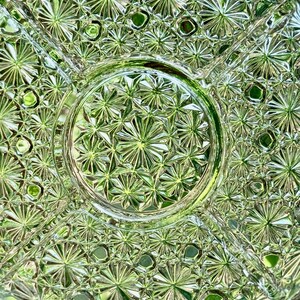 May include: Close-up of a clear, vintage glass serving dish with a starburst pattern. The dish is divided into sections and has a circular center. The intricate design reflects light, creating a sparkling effect. The dish is likely used for serving snacks or appetizers.