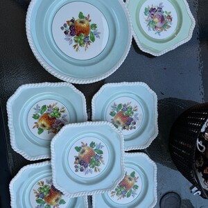 Puede incluir: Juego de siete platos de cer&aacute;mica vintage con fondo azul claro y borde de cuerda blanca. Los platos presentan un dise&ntilde;o floral con frutas y bayas en el centro.