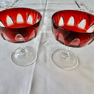 May include: Two clear glass stemmed dessert dishes with a red, cut-glass bowl. The bowls have a scalloped edge and a clear glass stem.