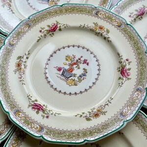 Puede incluir: Juego de platos de cer&aacute;mica blanca vintage con un patr&oacute;n floral verde y dorado. Los platos tienen un borde festoneado y un dise&ntilde;o central con un motivo floral.
