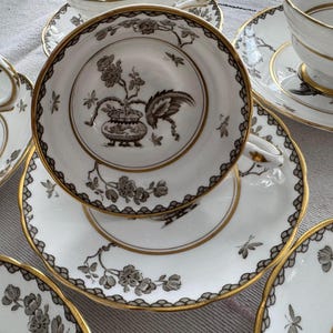 May include: A set of four vintage teacups and saucers with a black and gold floral pattern. The cups and saucers have a delicate, feminine design.