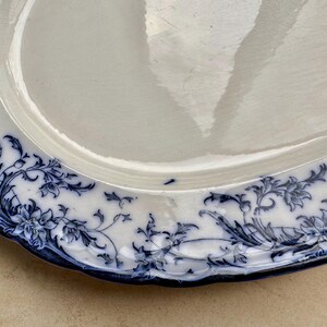 Puede incluir: Plato ovalado blanco antiguo con un dise&ntilde;o floral azul alrededor del borde. El patr&oacute;n presenta flores y follaje estilizados. El borde del plato tiene un dise&ntilde;o festoneado. Una pieza cl&aacute;sica para servir.