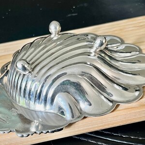 May include: A silver shell-shaped dish with a scalloped edge and three feet. The dish is marked "STERLING" and "INTERNATIONAL SILVER CO."