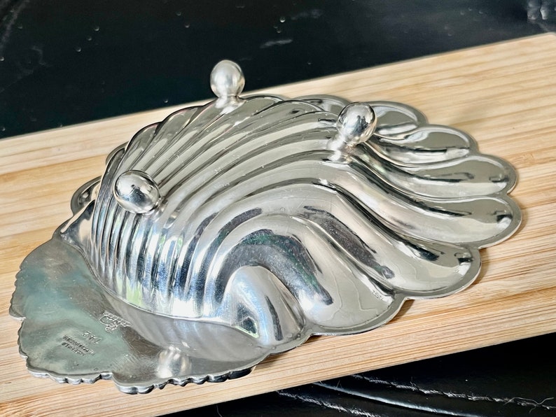 May include: A silver shell-shaped dish with a scalloped edge and three feet. The dish is marked "STERLING" and "INTERNATIONAL SILVER CO."